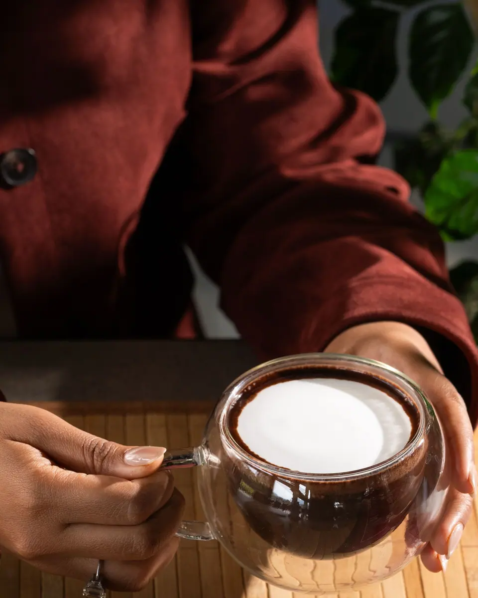 Hands cradle a double-walled glass of latte