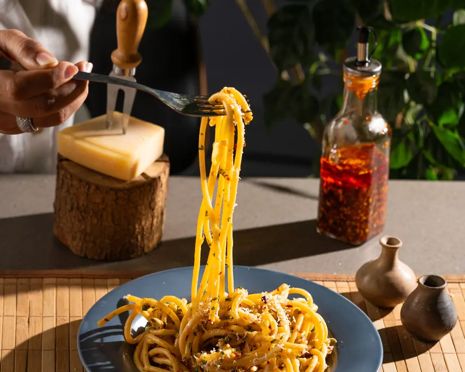 A fork lifts spaghetti from a blue plate, a block of parmesan behind
